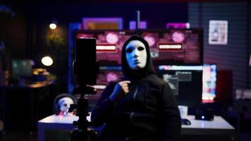 Focus on camera on phone on tripod used by hacker concealing identity filming ransom in hidden base. Close up of smartphone used by cybercriminal with mask to record blackmail footage, camera B video