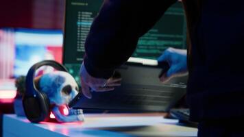 Hooded script kiddie taking laptop out of suitcase, prepared to launch DDoS attack. Close up shot of scammer at computer desk getting notebook from bag, starting work on malware script, camera A video