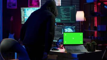 Hacker in hidden place using green screen laptop to deploy malware on unsecured devices, stealing sensitive data from unaware users online and selling it on black market, camera A video