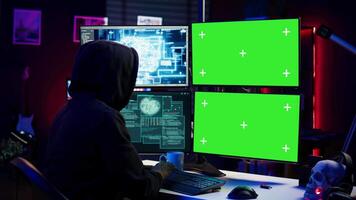 Hacker using AI and green screen computer monitors to produce malicious malware corrupt company data. Evil man working on mockup desktop PC using artificial intelligence, infecting systems, camera B video