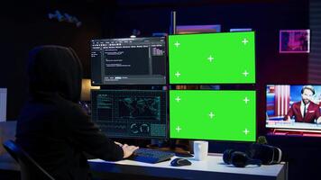 Hooded man writing lines of code on green screen PC from apartment, trying to get past security systems. Evil hacker using mockup computer to make scripts that can hack devices, camera B video