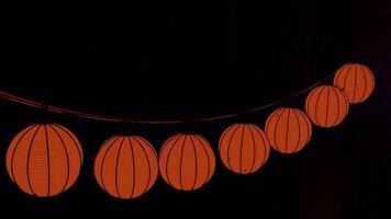 Halloween pumpkin garland hanging isolated on a black background. Design. Unusual orange lanterns in a form of a pumpkin swaying in the wind under the rain drops. video
