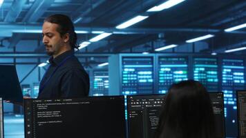 Manager overseeing server room, running code on laptop, troubleshooting and upgrading technologically advanced hardware clusters. System administrator programming in server farm video