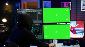 Hooded man writing lines of code on green screen PC from apartment, trying to get past security systems. Evil hacker using mockup computer to make scripts that can hack devices, camera A video