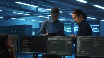 Multiracial team of technicians working in high tech server hub capable of storing vast amounts of data. Coworkers doing brainstorming, trying to troubleshoot servers controlling network resources video