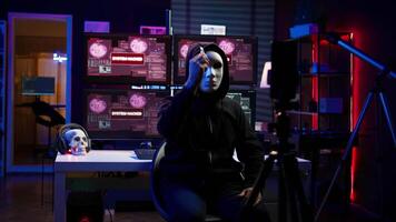 Hacker group member wearing anonymous mask filming threatening another country government to steal military secrets, doing international espionage in hidden underground base, camera B video
