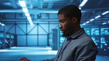 African american IT expert in server farm ensuring valuable data remains shielded from threats. Man safeguarding data center hardware against unauthorized access and vulnerabilities, securing system video