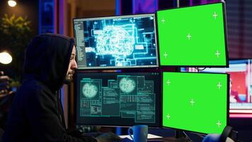 Hacker using AI and green screen computer monitors to produce malicious malware corrupt company data. Evil man working on mockup desktop PC using artificial intelligence, infecting systems, camera A video