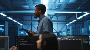 Technician doing system analysis using tablet, doing needed adjustments in supercomputers server farm. Engineer overseeing data center housing storage infrastructure supporting critical IT workloads video