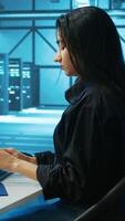 Vertical System administrator at PC desk working in computer network security data center, ensuring optimal performance. Employee monitoring energy consumption across operational server rigs components video
