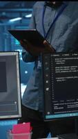 Vertical Technician in server hub using tablet to find hardware misconfigurations affecting rackmounts performance. Man checking data center infrastructure devices bottlenecks leading to errors video