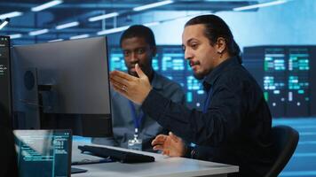 Team of technicians working together and laughing, supervising server rows in computer network security data center. Multiethnic colleagues having fun each other while overseeing supercomputers video