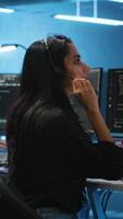 Vertical Woman talking in headphone mic, doing system analysis of server farm supercomputers. IT support worker in remote call using headset microphone in data center housing storage infrastructure video