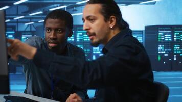 Upbeat african american computer scientist and coworker upgrading equipment in data center. Joyous admin at PC desk in high tech facility overseeing server clusters helped by colleague video