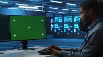 African american software developer coding on green screen computer, upgrading equipment. System administrator at PC desk overseeing server clusters using chroma key monitor video