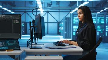 Computer scientist working in high tech server hub capable of processing vast amounts of data. Woman at PC desk typing on keyboard, updating servers controlling network resources video