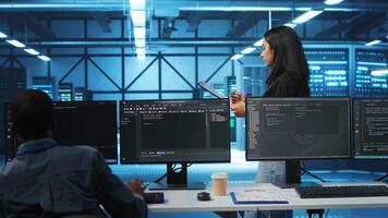 Indian manager in data center doing inspection on electronics and workers, ensuring order. Team leader reading clipboard files, supervising employees in server room infrastructure components video
