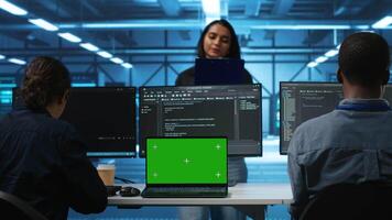 Green screen laptop in data center in front of manager and IT support specialists working together, supervising server rows. Team leader and employees overseeing supercomputers using mockup notebook video