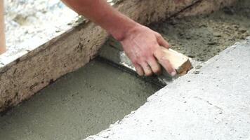 Construction, Worker Hands smooth wet cement in wooden frame at a construction site during daytime to ensure an even surface video