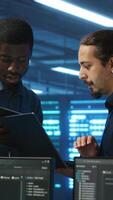 Vertical Coworking system administrators in server hub monitoring data center energy consumption across hardware using tablet. Colleagues inspecting supercomputers, ensuring malfunctions are fixed video