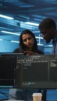Vertical Multiethnic team of engineers uses laptop to do programming for servers providing computing resources for different workloads. Diverse colleagues using notebook to supervise data center supercomputers video