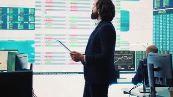 Chief executive officer reviews data shown on big display in the office, screens with infographics, finance analysis and organizational progress. Telecommunications system control room. Camera A. video