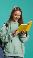 Vertical Young girl reading book, enjoying hobby, being entertained, isolated over studio background. Upbeat woman with novel in arms relaxing, having fun with interesting story, camera B video