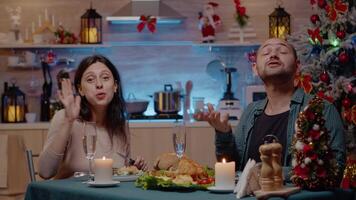 Couple talking on call conference enjoying festive dinner for winter holiday. Man and woman using online remote communication with family on christmas eve while having food and alcohol. video