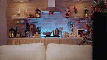Close up of kitchen counter decorated with christmas ornaments and cooking utensils. Empty room with couch and holiday decorations for celebration. Nobody in space with sofa and tree video