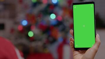 Close up of hand vertically holding smartphone with green screen. Woman looking at chroma key on device with isolated background and mockup template on christmas eve festivity. video