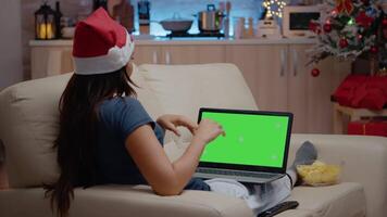 Woman talking and using horizontal green screen on laptop. Adult with santa hat watching isolated template and mockup background on gadget with chroma key. Device with technology video
