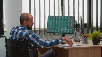 Disabled businessman sitting in wheelchair immobilized checking financial economy data taking notes in business office discussing with colleague. Handicapped freelancer using modern technology. video