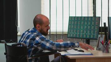 Paralysed manager in wheelchair comparing financial data from documents with colleague working financial corporate building using modern technology. Handicapped disabled businessman analysing graphs video