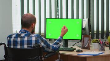 Immobilized businessman in wheelchair using computer with chroma key for videomeeting. Handicapped disabled freelancer looking at pc with green screen, mockup, key talking with remotely colleagues video