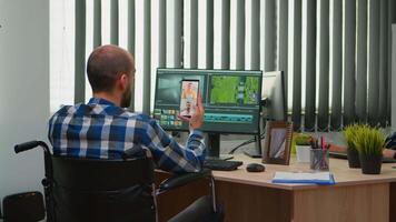 Handicapped videographer in wheelchair talking on webcam with cowerkers while editing a project creating content in modern company office. Creator blogger working from photo studio. video