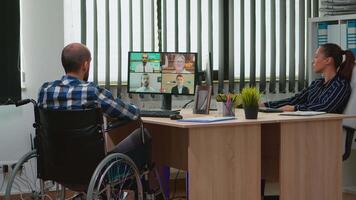 Paralysed, immobilized freelancer in wheelchair having videomeeting discussing online with coworkes in business office. Handicapped businessman working in financial company using modern technology. video