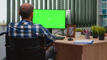 Handicapped disabled freelancer looking at pc with green screen talking with colleagues. Immobilized businessman in wheelchair using computer with chroma key, mockup, greenscreen for videomeeting. video