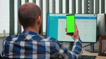 Immobilized businessman in wheelchair using smartphone with greenscreen for videomeeting. Handicapped disabled freelancer looking at display with chroma key, mockup talking with remotely colleagues video