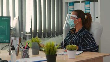 Businesswoman with visor and protection mask working in new normal business office. Freelancer discussing with colleague in financial company respecting social distance during global pandemic. video