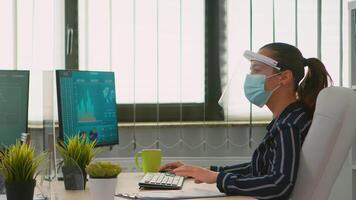 Manager woman wearing face protection against coronavirus typing on computer analysing new statistics data working in new normal financial office. Freelancer in company respecting social distance. video