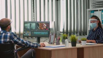 Team of videographers with protection masks working at project creating content, man blogger sitting in wheelchair in new normal office. Disabled freelancer editing durig global pandemic video