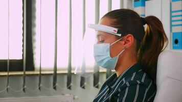 Portrait of businesswoman wearing protection mask and visor typing and talking with colleague working in new normal business office respecting social distance during global pandemic. video