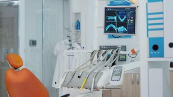 Close up revealing shot of medical orthodontist monitor with teeth x ray images on it. Empty modern clinic stomatology chair with nobody in it. Professional dentistry equipment with dental tools video