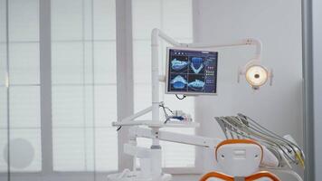 Close up of medical orthodontist display with teeth x ray images on it. Empty professional hospital office stomatology chair with nobody in it. Closeup of dental drill instrument ready for tooth care video