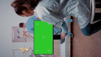 Vertical . Specialist using green screen on monitor in dentistry cabinet. Dentist working with chroma key and isolated mockup template on computer for dental care and stomatology video