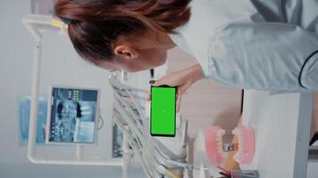 Vertical . Specialist analyzing mobile phone with green screen for dental care. Dentist holding smartphone with chroma key on display for isolated background at stomatology clinic video