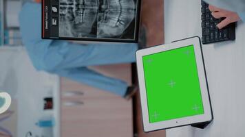Vertical . Close up of horizontal green screen on digital tablet at dentist office. Stomatologist using mockup template and isolated background on gadget for dentistry and oral care video