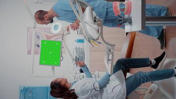 Vertical . Dentist and assistant working with green screen on display while discussing oral care examination. Woman and man using chroma key with mockup template and isolated background on monitor video