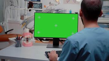 Man looking at computer with horizontal green screen for dentistry at cabinet. Assistant working with chroma key and isolated background on monitor for stomatological care and checkup video