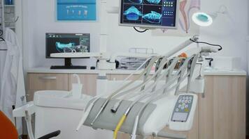 Closeup revealing shot of medical orthodontic display with teeth xray images on it. Stomatology dental chair with nobody in it equipped with dentistry tools prepared for orthodontic healthcare surgery video